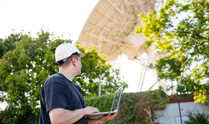 Engineer testing earth based astronomical radio telescope use laptop. Radio telescopes used in science for space observation and distant objects exploring. Big satellite dishes